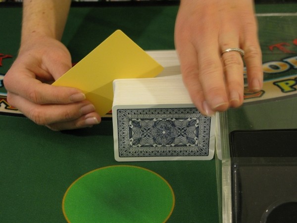 The dealer is putting a yellow cut card in a deck of 8